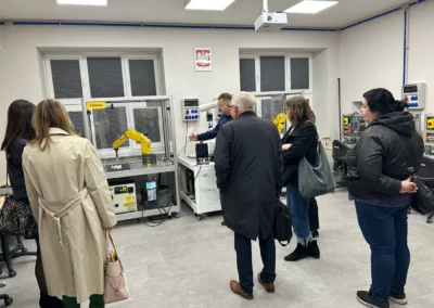 Uczestnicy spotkania obserwują stanowiska dydaktyczne i robota przemysłowego podczas wizyty w BCU Nr 2 w Radomiu